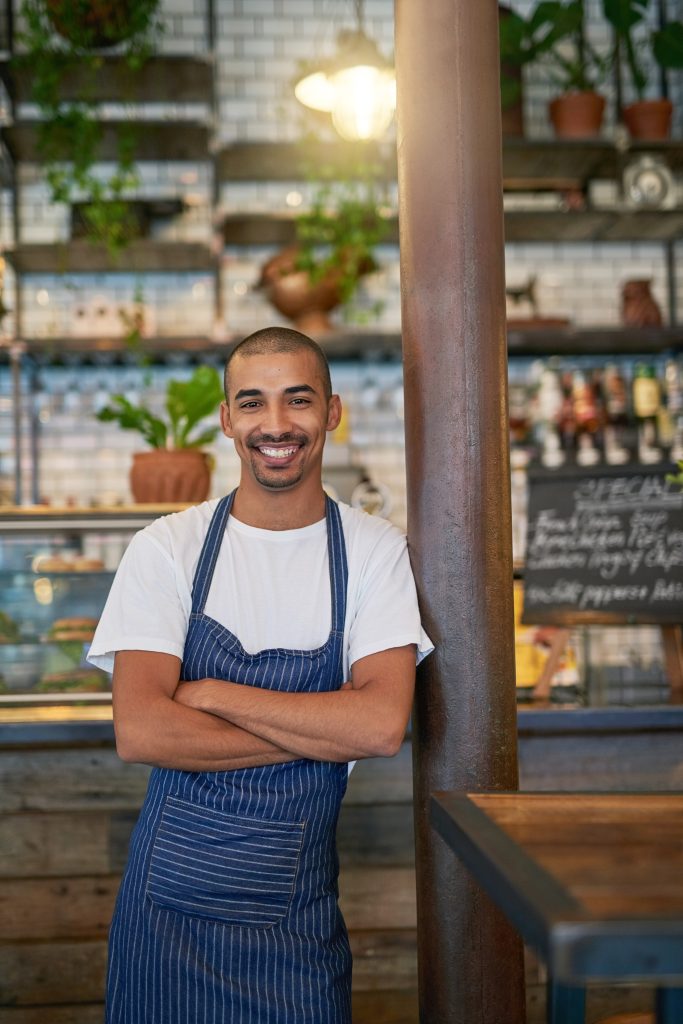 Cafe, man and business or happy portrait, entrepreneur and crossed arms and proud for startup. Coffee shop, restaurant or smile with owner for hospitality service, workplace for profession and work.